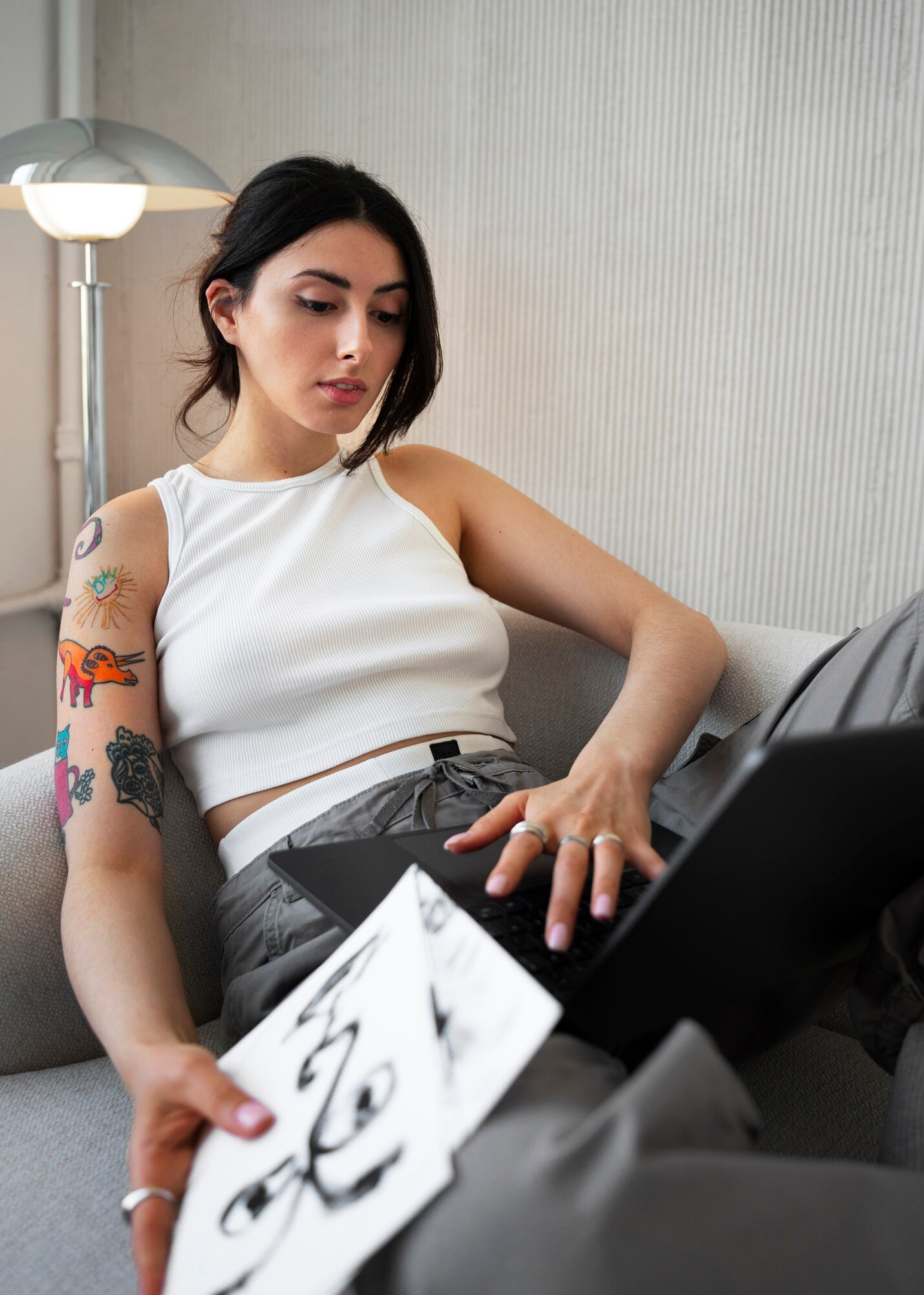 Garota sexy tatuada no sofá com notebook no colo trabalhando remotamente, linda jovem, braço tatuado, home office freelancer