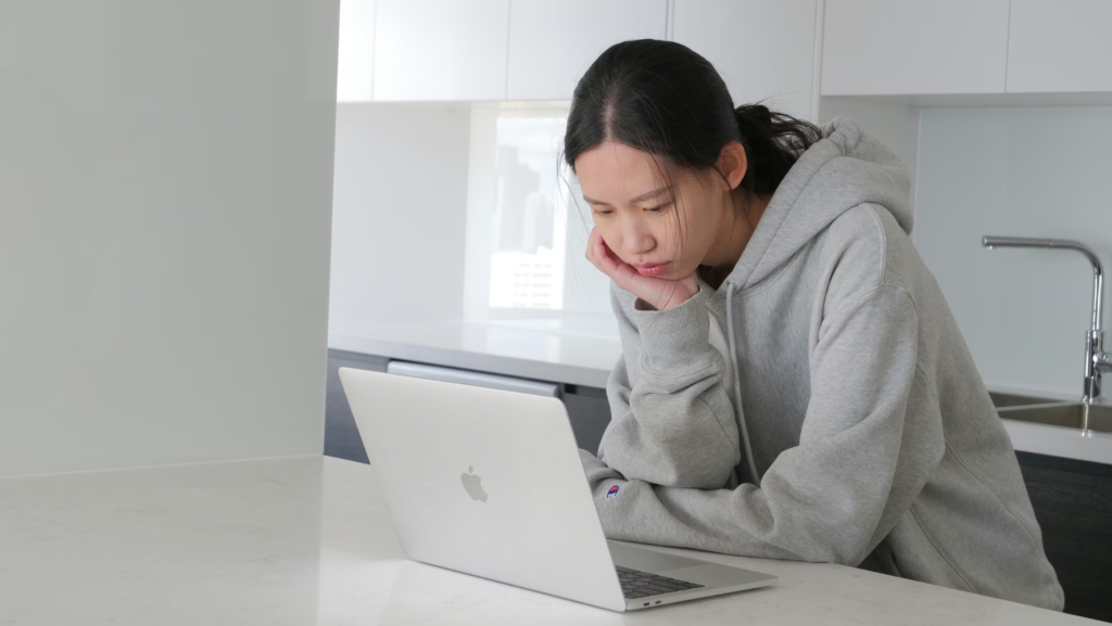 Mulher jovem usando o notebook sobre a mesa com a cabeça inclinada.